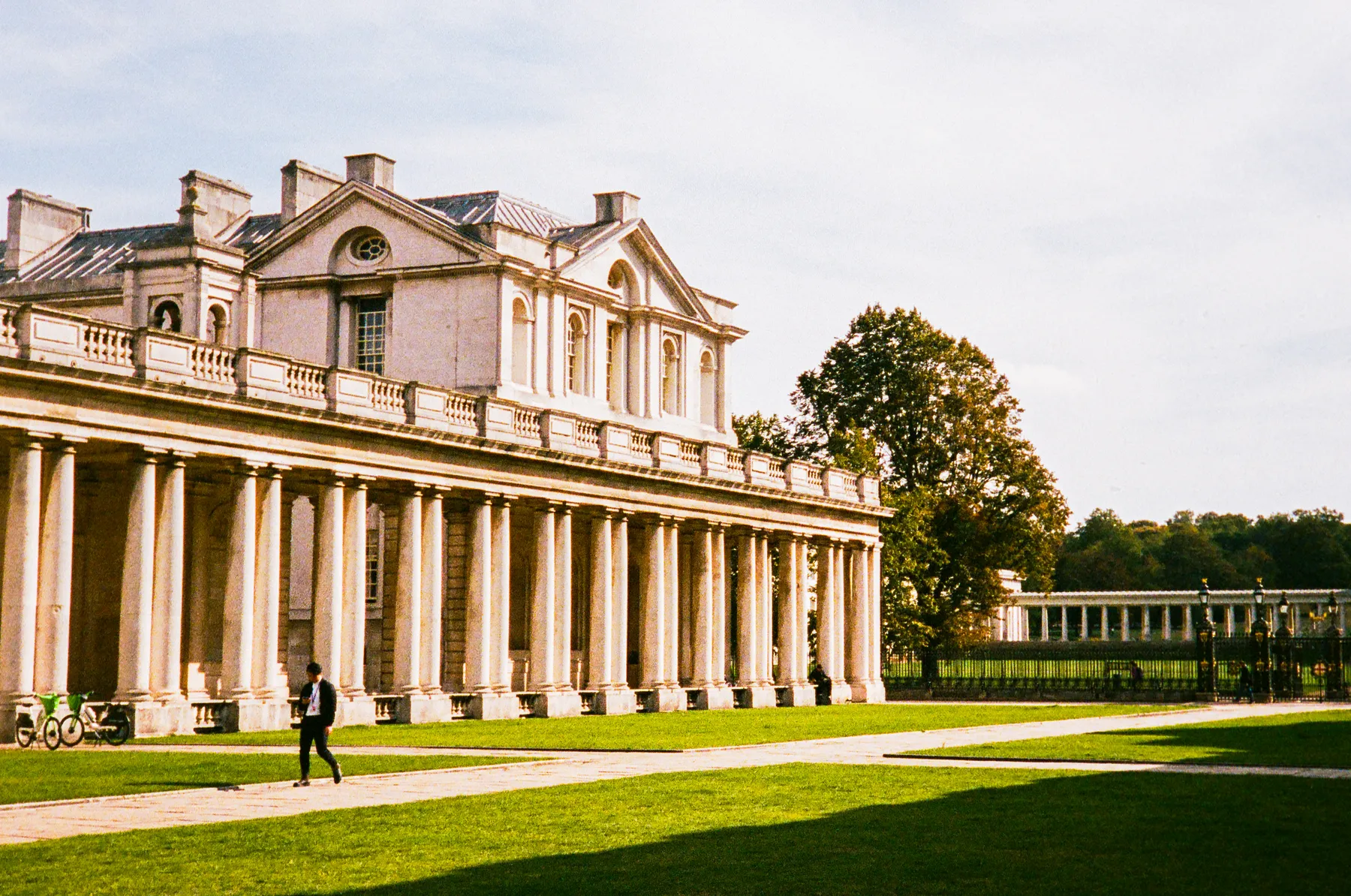 a lone figure walking past the colonnade of the old royal naval college, greenwich