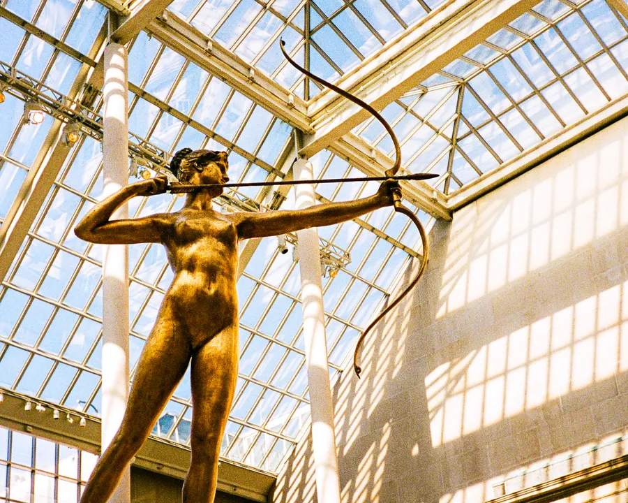the gilded statue of diana drawing her bow beneath the glass roof of the met