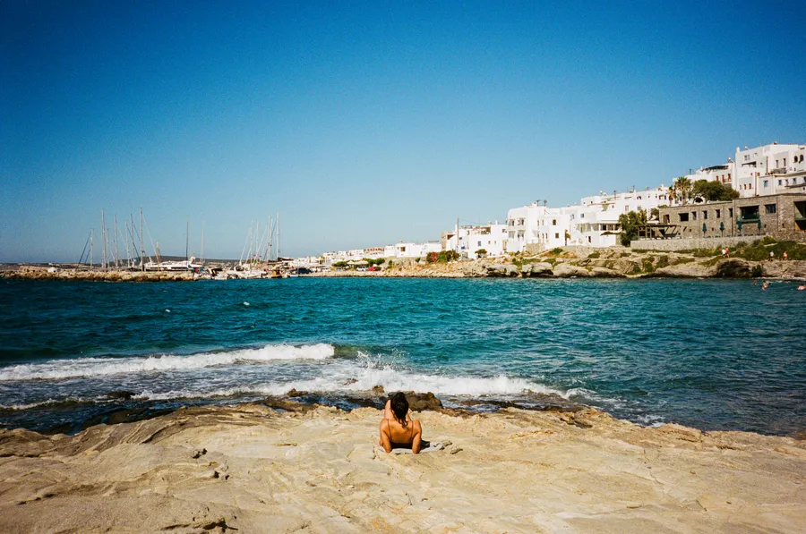a sunbather on pale rocks above a churning teal sea, paros