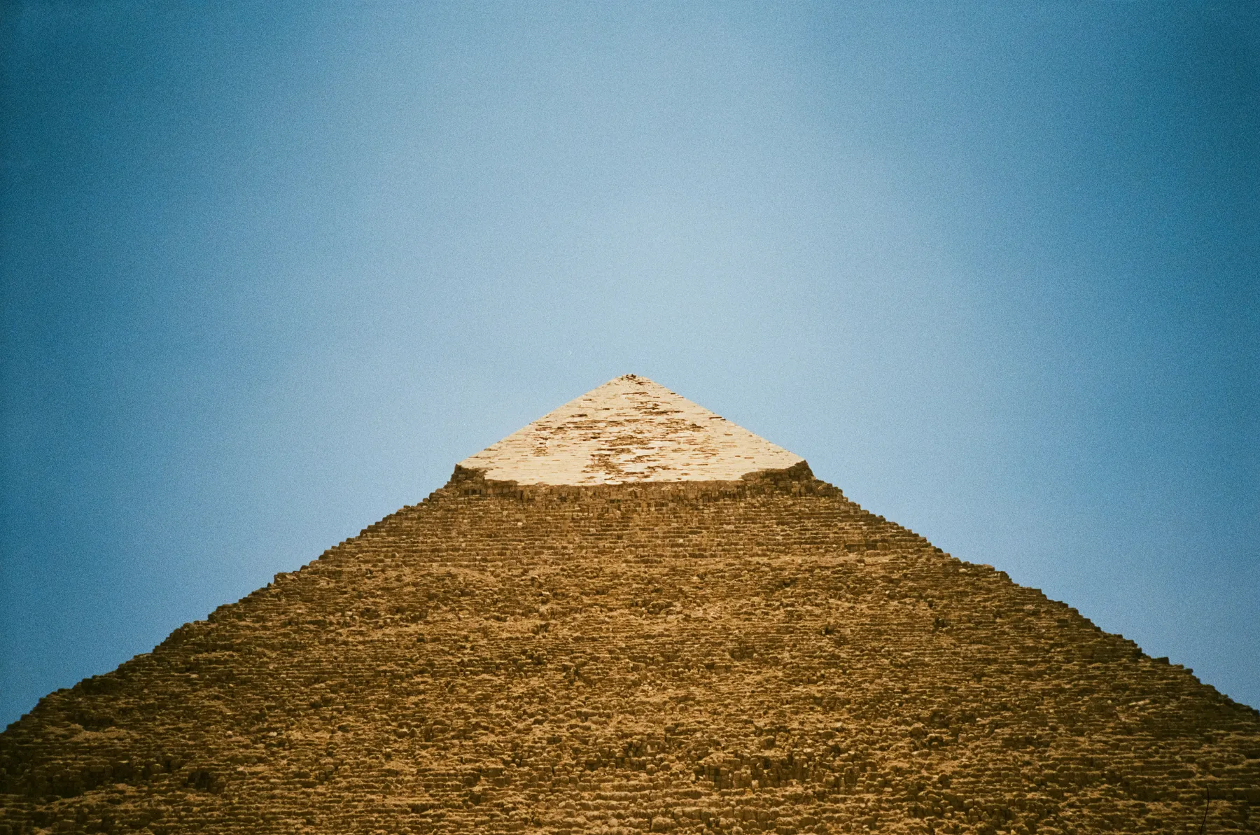 the great pyramid of giza rising against a deep blue sky, seen from its base