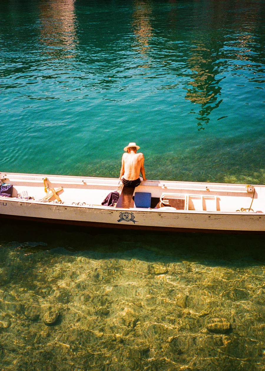 a man standing in a long boat on clear turquoise water, zürich