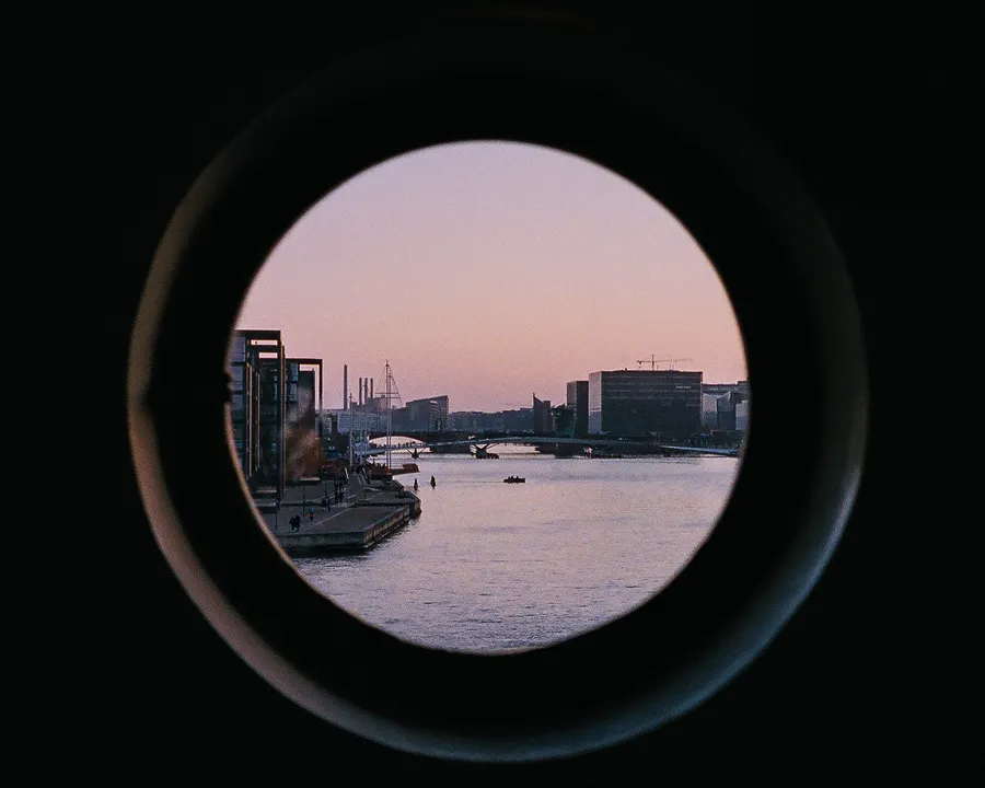 the harbour of copenhagen at dusk, seen through a round porthole window